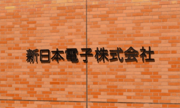 レンガ壁に掲示された新日本電子株式会社の社名サイン