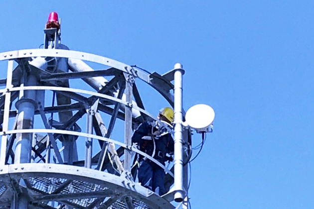 設計図を囲んで打ち合わせをするエンジニアチームと作業服の技術者たち